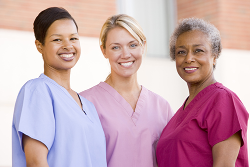 Three female nurses standing outside wearing different color scrubs