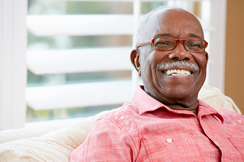 African American man wearing glasses and red shirt smiling sitting on white couch