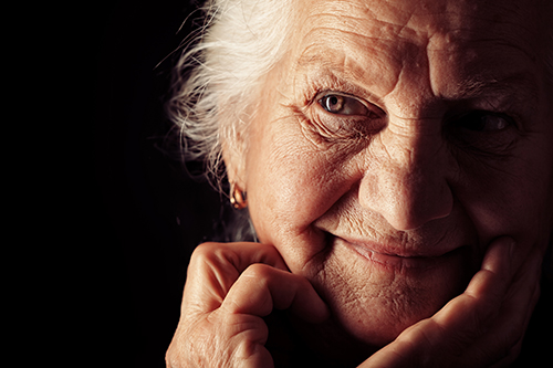 Close of up elderly woman smiling with bright brown eyes, dark background